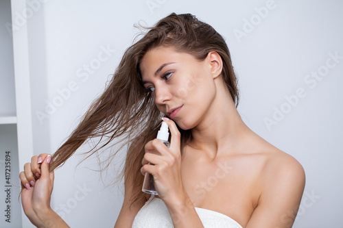 Young woman applying oil onto hair in bathroom