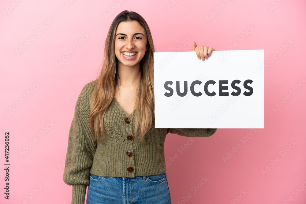 Young caucasian woman isolated on pink background holding a placard with text SUCCESS with happy expression Young caucasian woman isolated on pink background holding a placard with text SUCCESS with happy expression