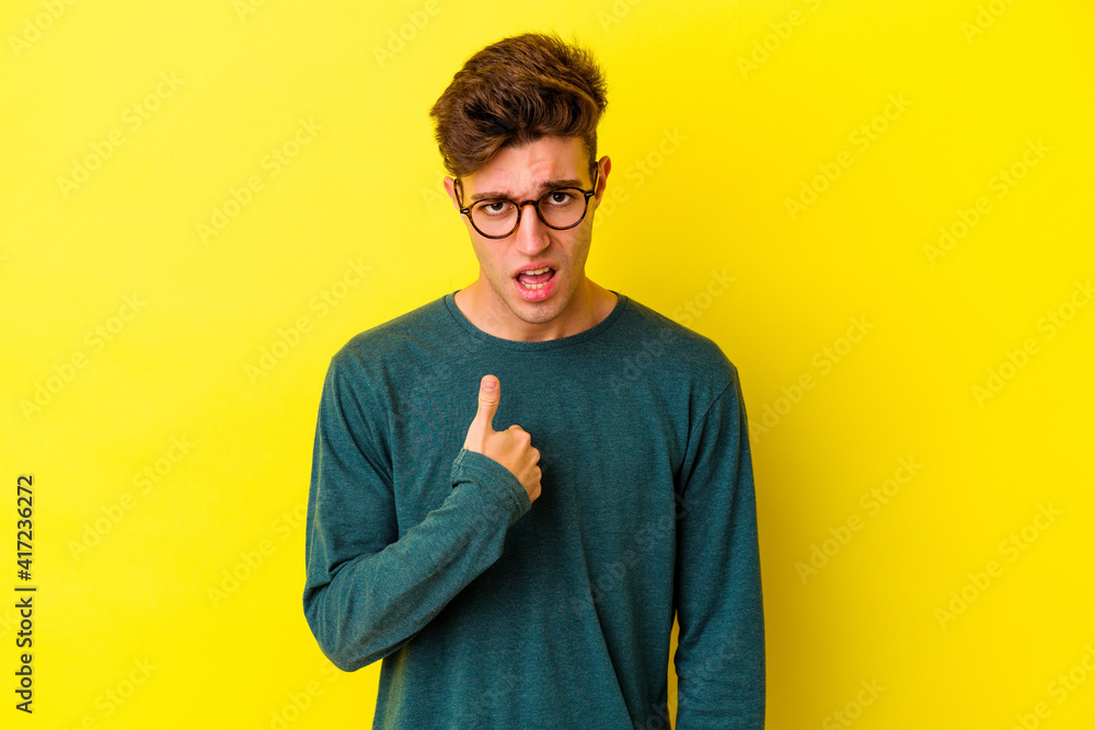 Young caucasian man isolated on yellow background surprised pointing with finger, smiling broadly. Young caucasian man isolated on yellow background surprised pointing with finger, smiling broadly.