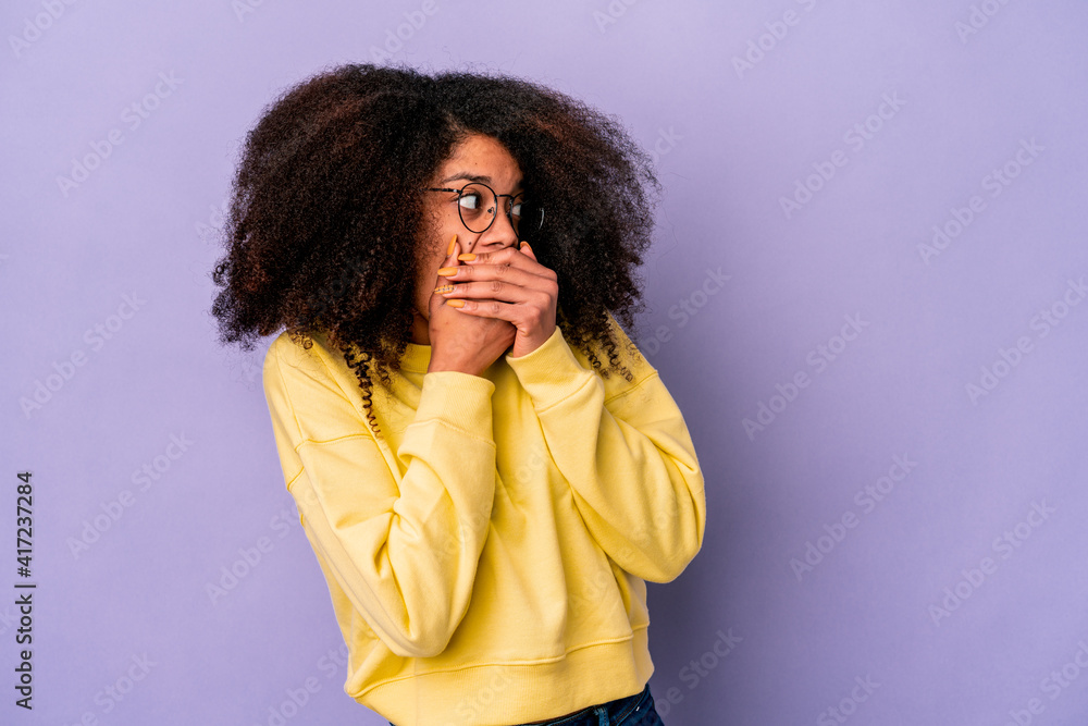 Young african american curly woman isolated on purple background thoughtful looking to a copy space covering mouth with hand. Young african american curly woman isolated on purple background thoughtful looking to a copy space covering mouth with hand.