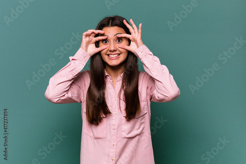 Young Indian woman isolated on blue background keeping eyes opened to find a success opportunity.