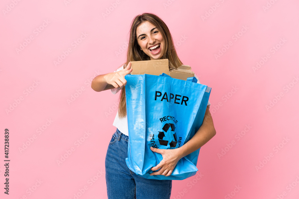 holding a recycling bag full of paper to recycle over isolated pink points finger at you holding a recycling bag full of paper to recycle over isolated pink points finger at you