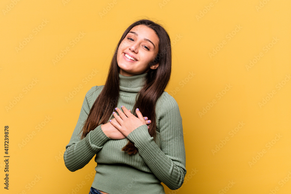 Young Indian woman isolated on yellow background has friendly expression, pressing palm to chest. Love concept. Young Indian woman isolated on yellow background has friendly expression, pressing palm to chest. Love concept.