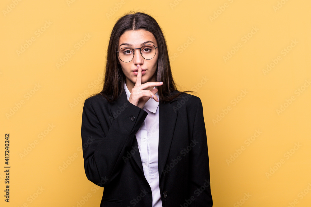 Young Indian business woman isolated on yellow background keeping a secret or asking for silence. Young Indian business woman isolated on yellow background keeping a secret or asking for silence.
