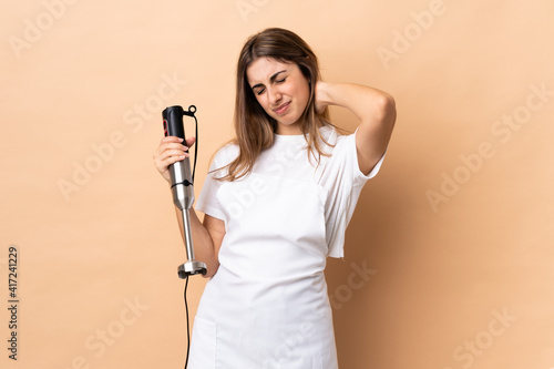 Woman using hand blender over isolated background with neckache