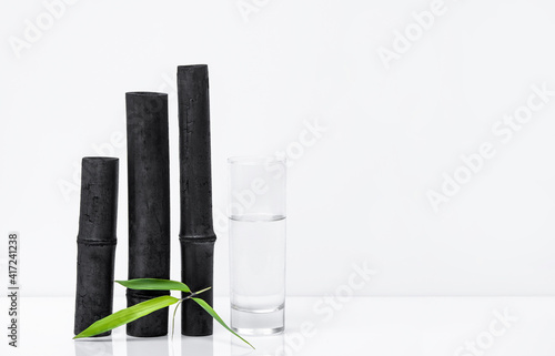 Bamboo charcoal water filter sticks, green leaf and glass of water. Natural bamboo charcoal is a powerful purifier which refreshes tap water photo