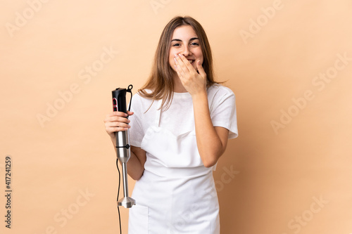 Woman using hand blender over isolated background happy and smiling covering mouth with hands