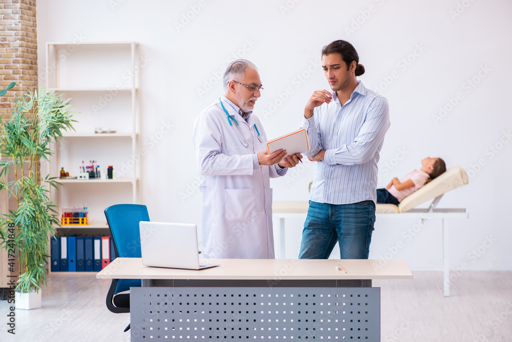 Fototapeta premium Small girl with her father visiting old male doctor