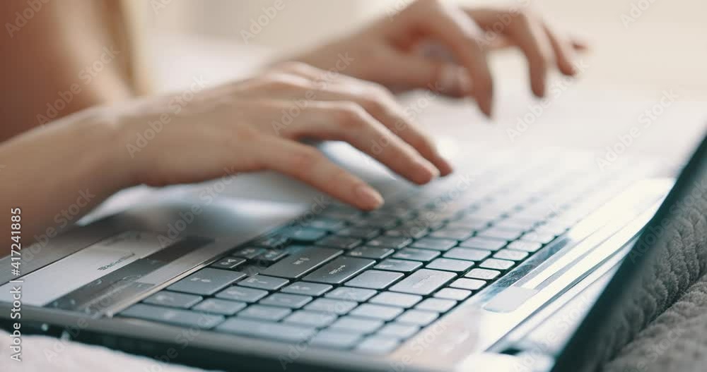 Female hands typing on laptop keyboard on bed at bedroom, close up view. Bright sunny light Female hands typing on laptop keyboard on bed at bedroom, close up view. Bright sunny light