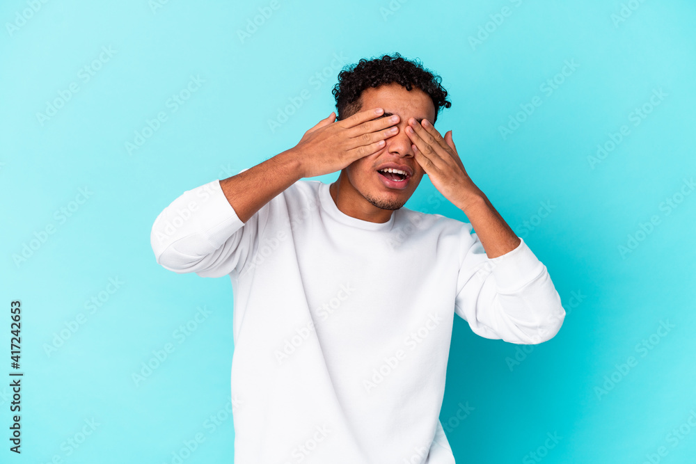 Young african american curly man isolated on blue afraid covering eyes with hands. Young african american curly man isolated on blue afraid covering eyes with hands.