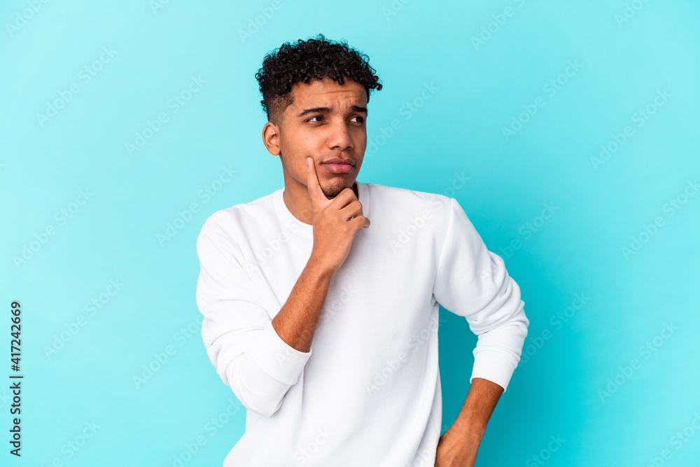 Young african american curly man isolated on blue contemplating, planning a strategy, thinking about the way of a business. Young african american curly man isolated on blue contemplating, planning a strategy, thinking about the way of a business.