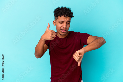 Young african american curly man isolated on blue showing thumbs up and thumbs down, difficult choose concept