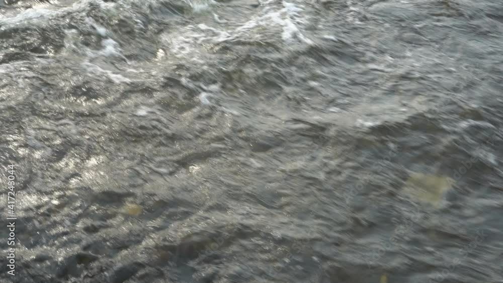 A look from above at the surface of a fast-moving river on a sunny spring day. Close-up of waves and swirls. Hypnotic movement of water. Surrealism. 4K