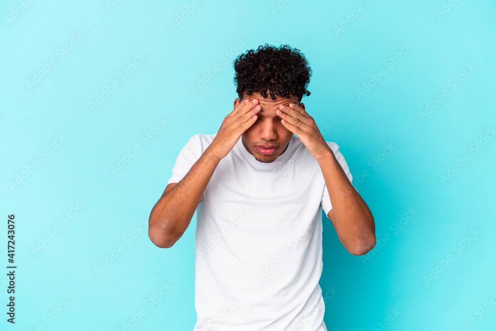 Young african american curly man isolated on blue having a head ache, touching front of the face. Young african american curly man isolated on blue having a head ache, touching front of the face.