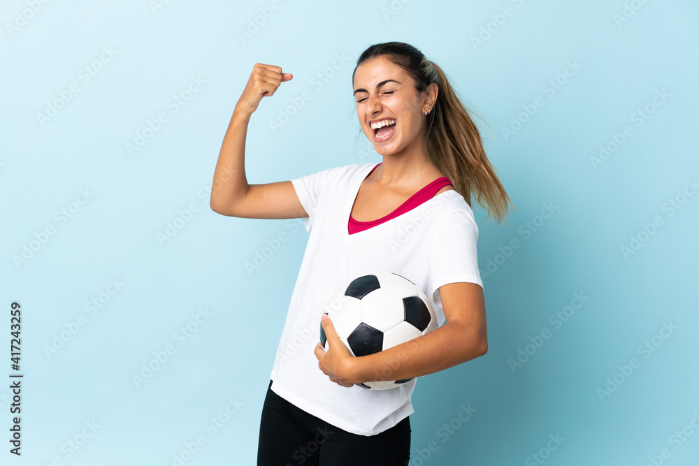 Young hispanic woman over isolated blue background with soccer ball celebrating a victory Young hispanic woman over isolated blue background with soccer ball celebrating a victory