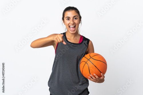 Young hispanic woman playing basketball over isolated white background surprised and pointing front © luismolinero