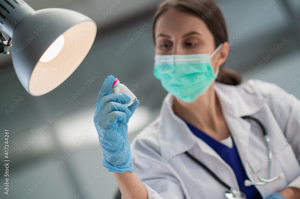 In the medical clinic, vaccination of the population against covid-19 has begun, the doctor shows a bottle with the vaccine. In the medical clinic, vaccination of the population against covid-19 has begun, the doctor shows a bottle with the vaccine.