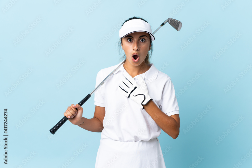 Young hispanic golfer woman over isolated blue wall surprised and shocked while looking right Young hispanic golfer woman over isolated blue wall surprised and shocked while looking right