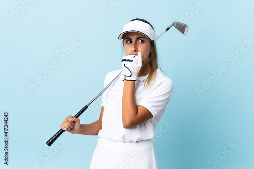 Young hispanic golfer woman over isolated blue wall having doubts