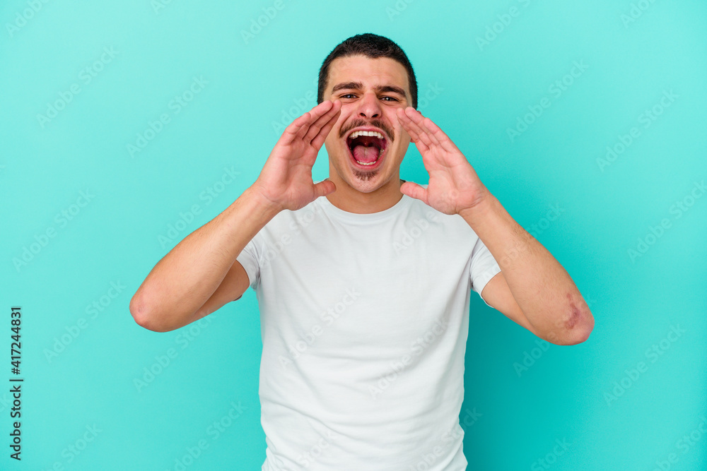 Young caucasian man isolated on blue background shouting excited to front. Young caucasian man isolated on blue background shouting excited to front.