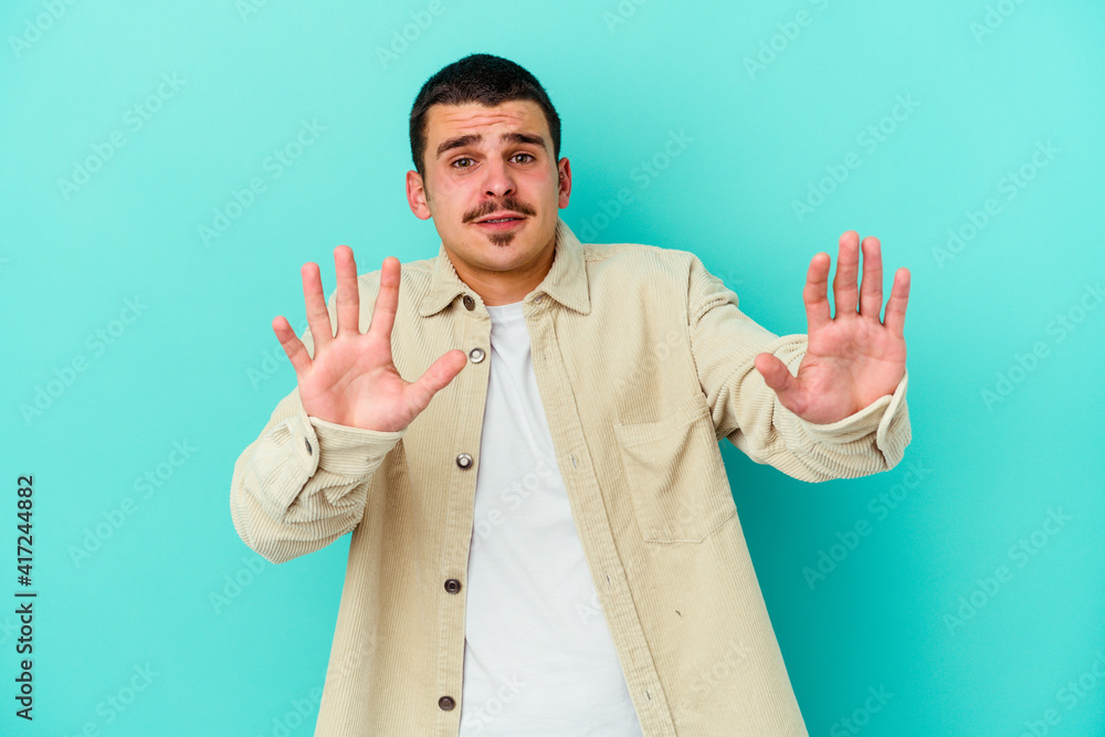 Young caucasian man isolated on blue background rejecting someone showing a gesture of disgust. Young caucasian man isolated on blue background rejecting someone showing a gesture of disgust.