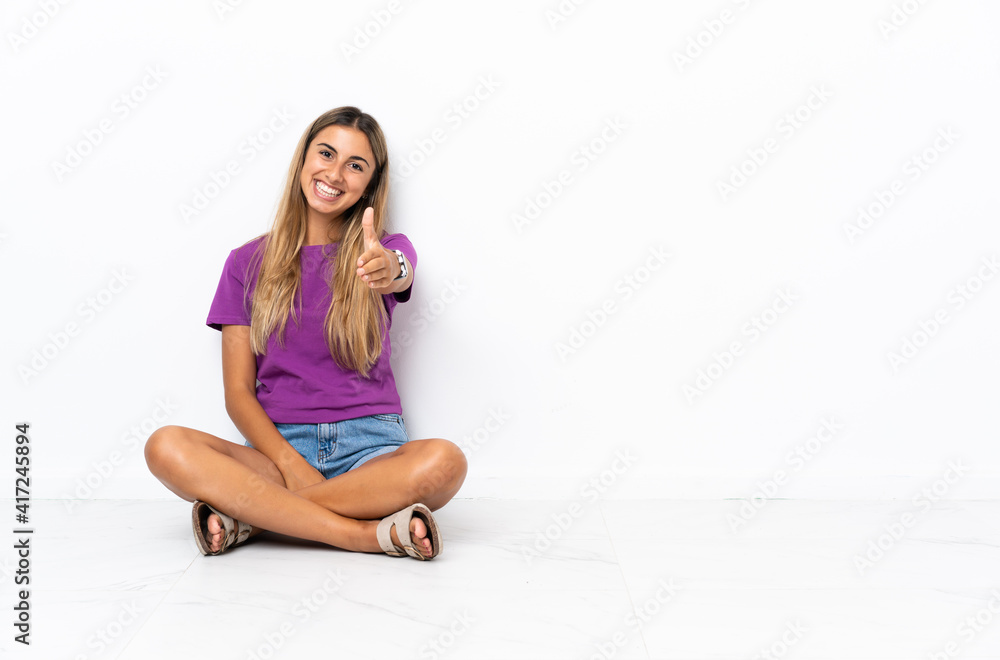 Young hispanic woman sitting on the floor shaking hands for closing a good deal Young hispanic woman sitting on the floor shaking hands for closing a good deal