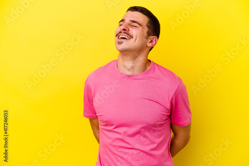 Young caucasian cool man isolated on yellow background relaxed and happy laughing, neck stretched showing teeth.