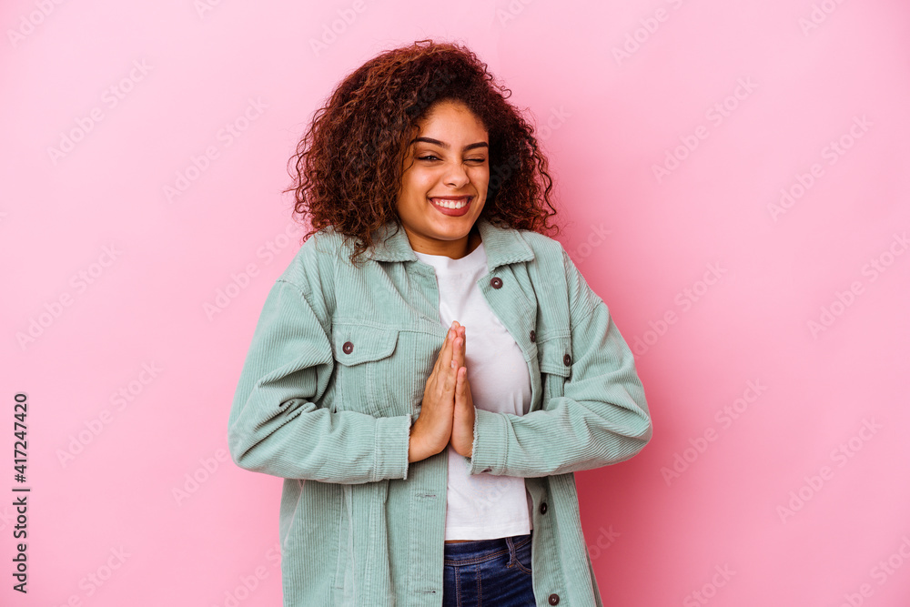 Young african american woman isolated on pink background holding hands in pray near mouth, feels confident. Young african american woman isolated on pink background holding hands in pray near mouth, feels confident.