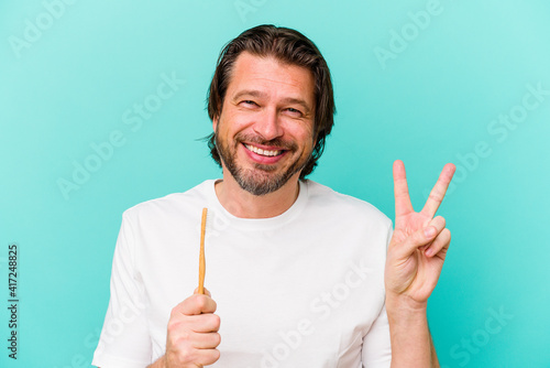 Middle age dutch man holding a toothbrush isolated on blue background joyful and carefree showing a peace symbol with fingers.