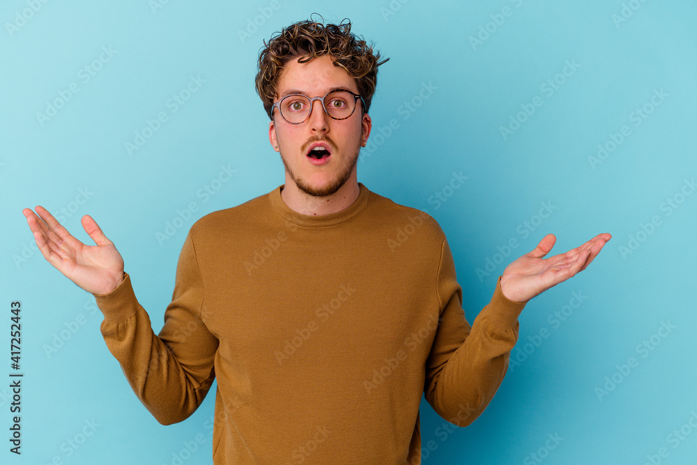 Young caucasian man wearing eyeglasses isolated on blue background surprised and shocked. Young caucasian man wearing eyeglasses isolated on blue background surprised and shocked.