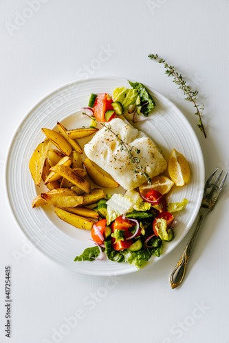 Oven baked chilean sea bass with herb roasted potatoes and fresh salad photo