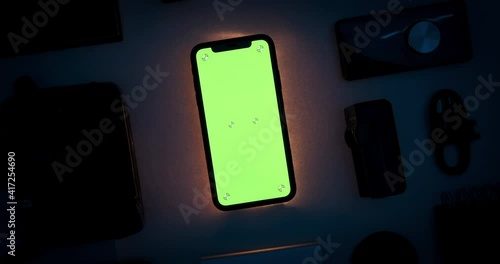 Phone chroma key green screen display mockup with tracking markers. Dark room interior with tech gadgets layout. Evening light scene with mobile illumination. Turning movement. 3D CGI close up 4k shot