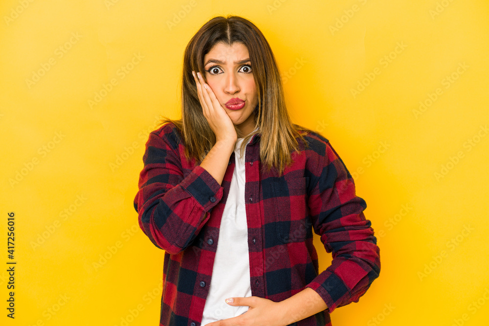 Young indian woman isolated on yellow background blows cheeks, has tired expression. Facial expression concept. Young indian woman isolated on yellow background blows cheeks, has tired expression. Facial expression concept.