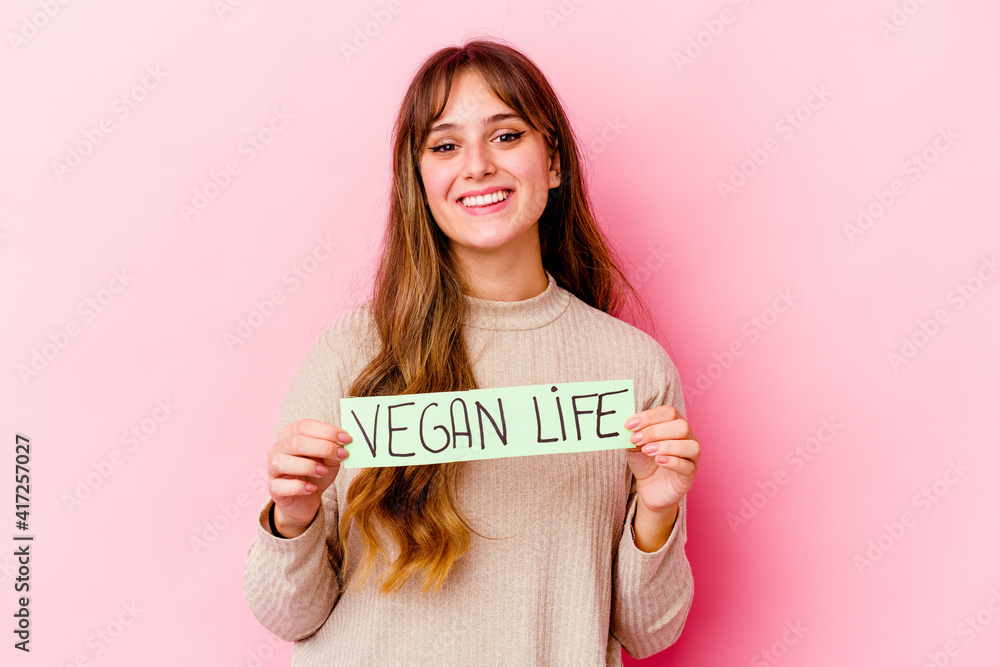 Young caucasian woman holding a vegan life placard isolated happy, smiling and cheerful. Young caucasian woman holding a vegan life placard isolated happy, smiling and cheerful.