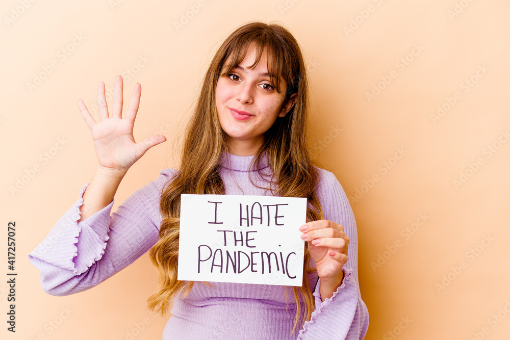 Young caucasian woman holding a I hate the pandemic placard isolated smiling cheerful showing number five with fingers. Young caucasian woman holding a I hate the pandemic placard isolated smiling cheerful showing number five with fingers.