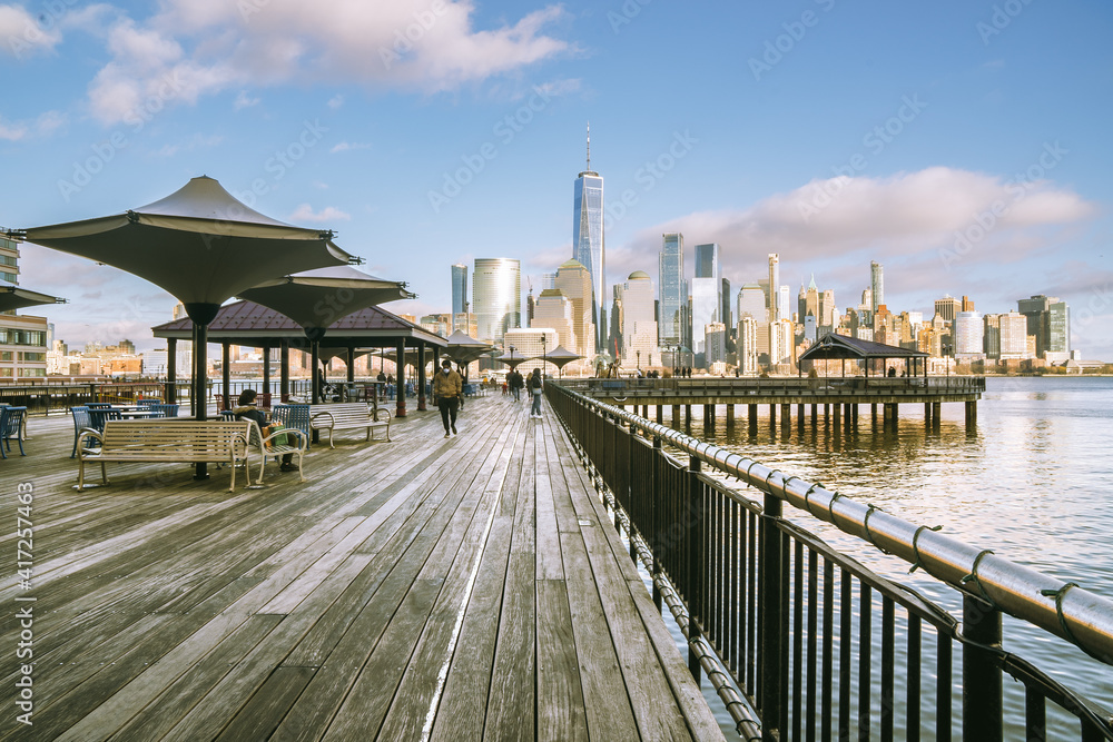 Jersey City, NJ - USA - Feb. 27, 2021: Landscape sunset view of people enjoying the riverfront at J Owen Grundy Park; with the lower Manhattan skyline in the distance,