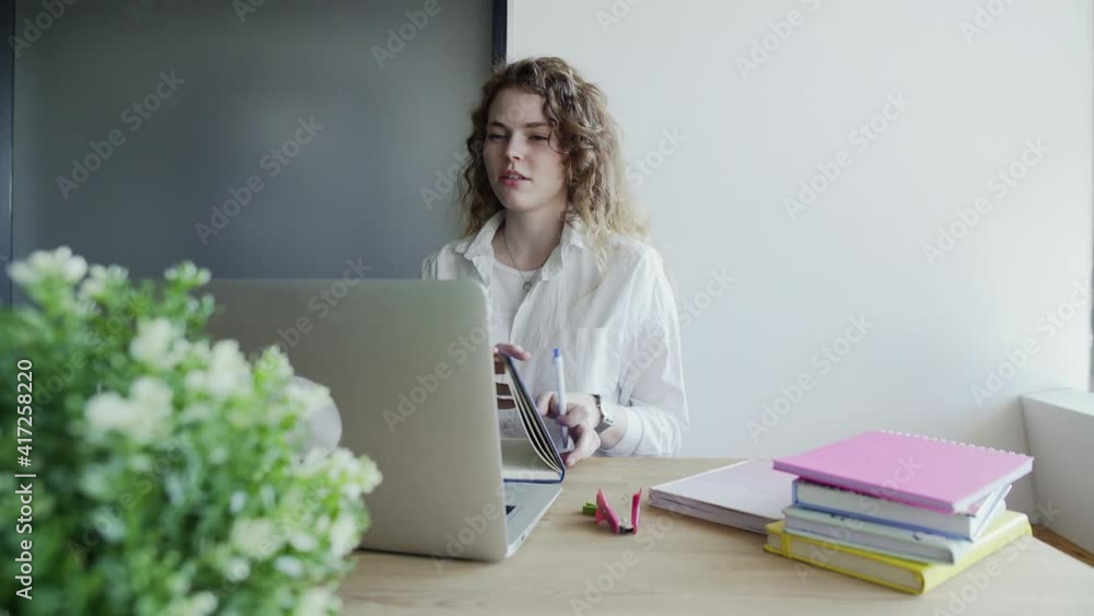 Young woman uses laptop to talks by video chat with her colleagues and makes notes Young woman uses laptop to talks by video chat with her colleagues and makes notes