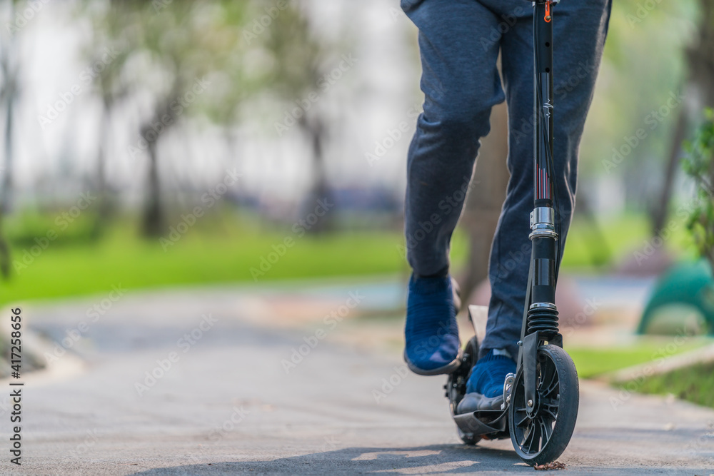 outdoors workout exercise background of man ridding on kick scooter on pavement in park outdoors workout exercise background of man ridding on kick scooter on pavement in park