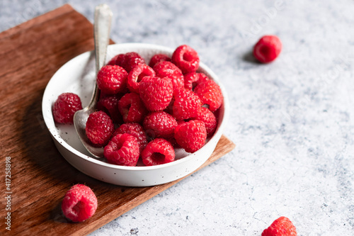 Fresh raspberries in a shallow dish with a spoon sitting on a cutting board. photo