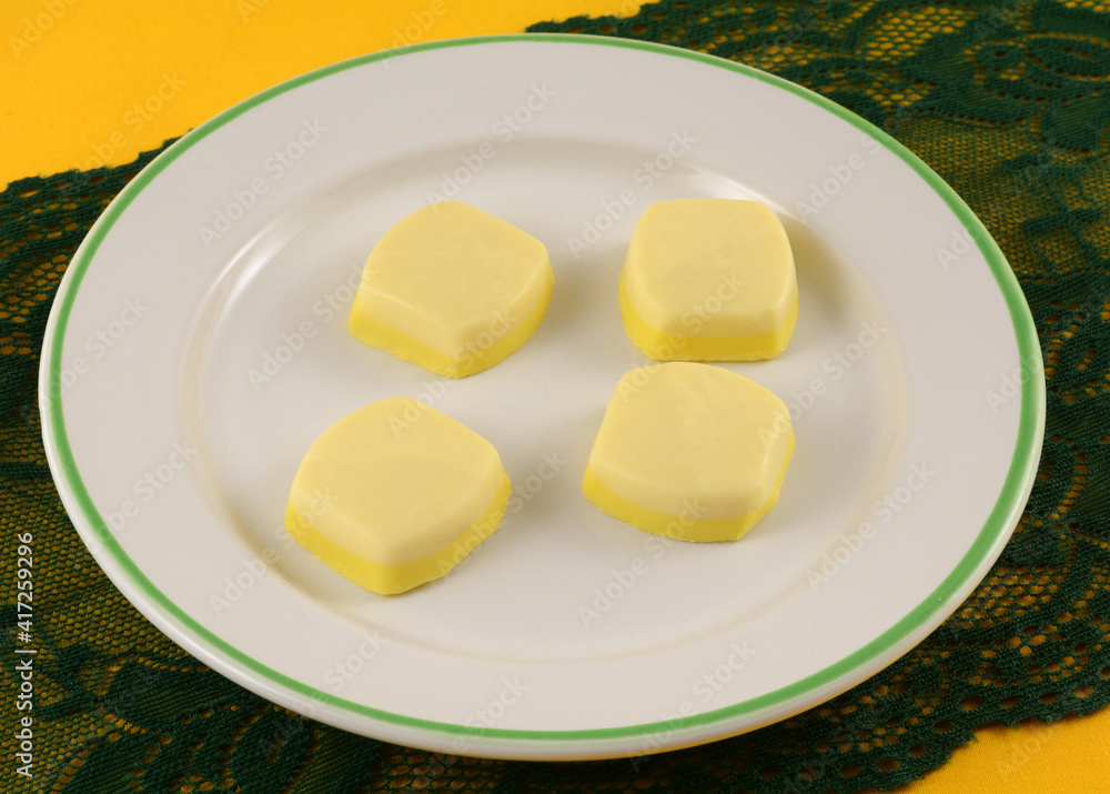 White chocolate and lemon meringue candy pieces on white dessert plate on green lace table runner on yellow tablecloth