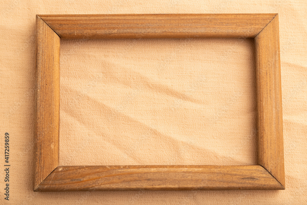 Fototapeta premium Wooden frame on smooth orange linen tissue. Top view, natural textile background.