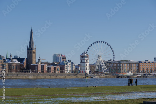 Outdoor sunny view, people chill out on natural park along riverside of Rhine River, and background of river and cityscape of Düsseldorf, Germany in winter season.