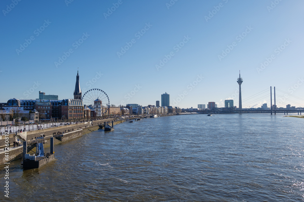 Outdoor panoramic sunny scenic cityscape view of Düsseldorf city, Germany, with promenade walkway on waterfront through old town and downtown, view from the bridge over Rhine River in winter. 