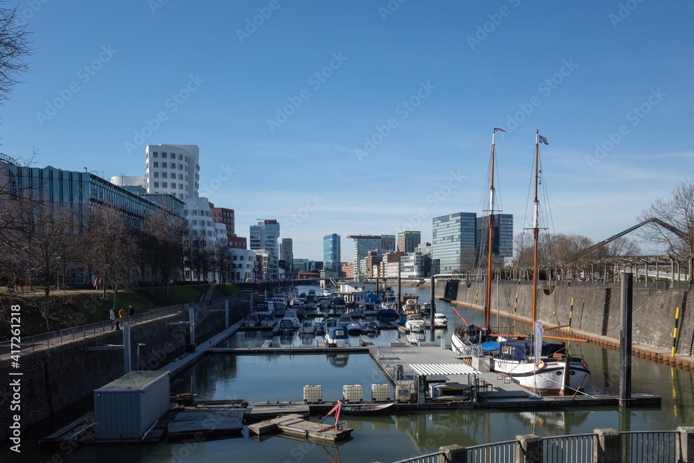 Outdoor scenery of Medienhafen harbour with many boats and yachts anchor at pier, surrounded with modern contemporary architectures.