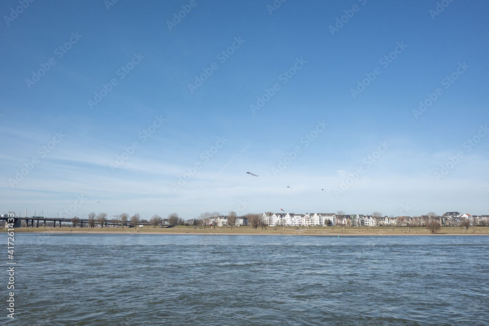 Outdoor sunny view of people play and fly kite on natural park field on riverside of Rhine River, and background of cityscape Düsseldorf, Germany.