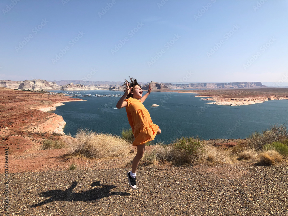 Young girl jumping for joy by desert lake on a sunny day in an orange dress