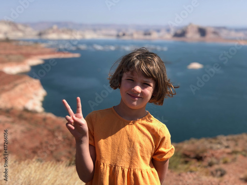 Young girl giving peace sign by desert lake on a sunny day in an orange dress