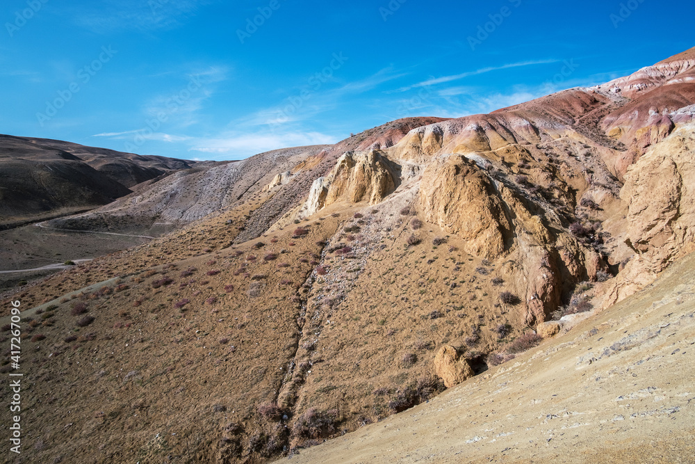 Large hills of red and yellow clay, traces of erosion, rocky surface and sparse vegetation.
