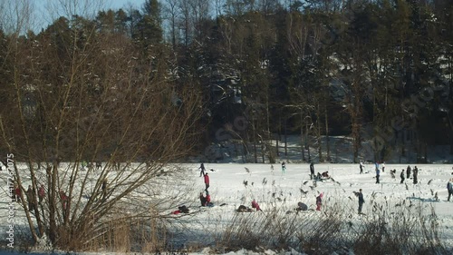 Picturesque view of crowd of people ice skating, enjoying Frozen Lhotka lake in Harasov, Kokorin, Czech Republic - Wide slow-motion panning shot photo