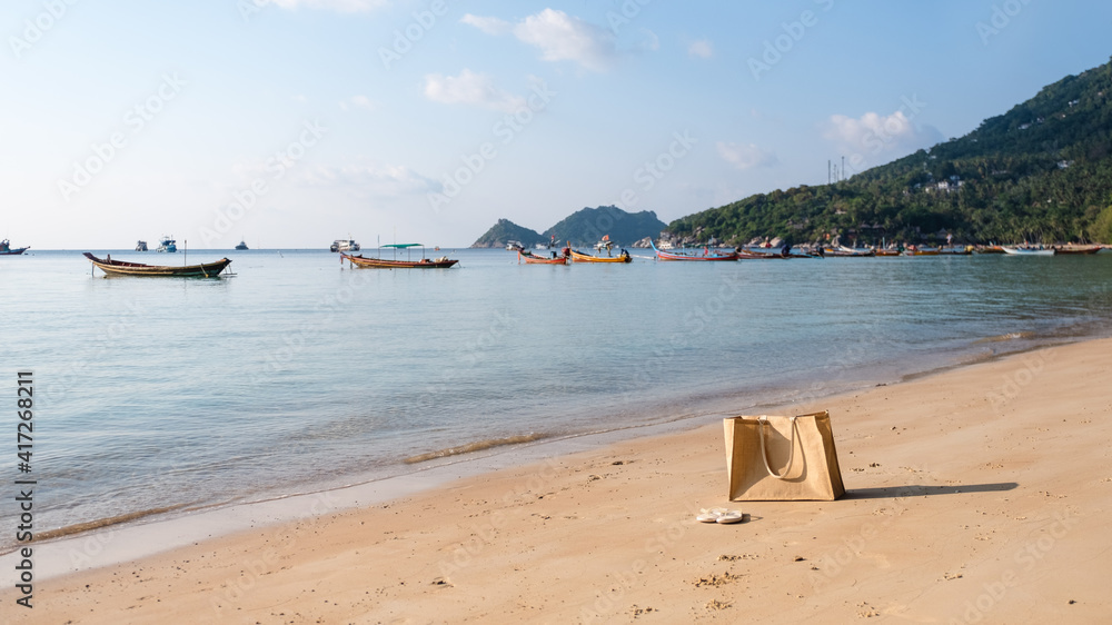 A bag and a pair of slippers on tropical white beach